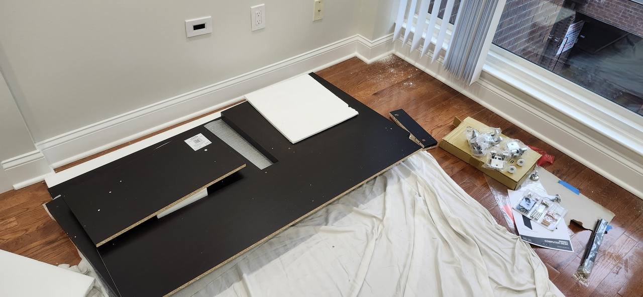 Flat-pack desk panels, metal runners and bagged hardware laid out beside a window