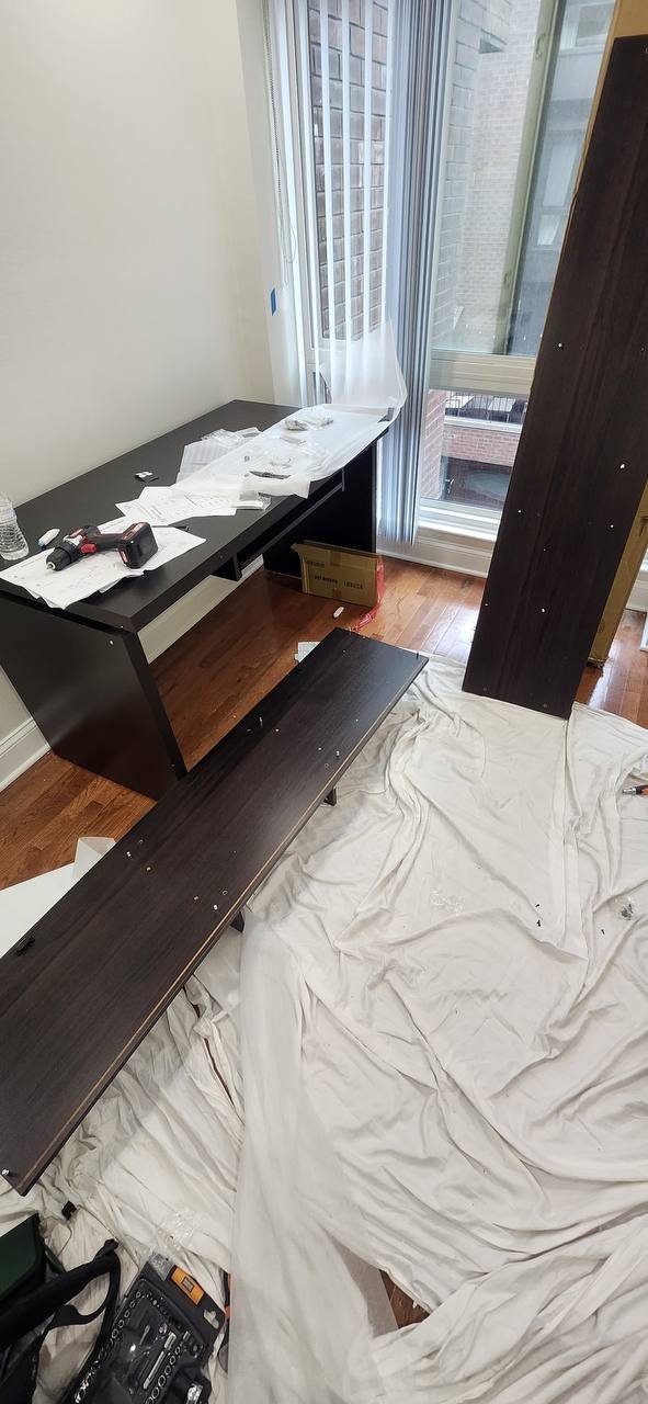 Partly assembled dark-finish computer desk with tools on top and loose panels on a protective sheet