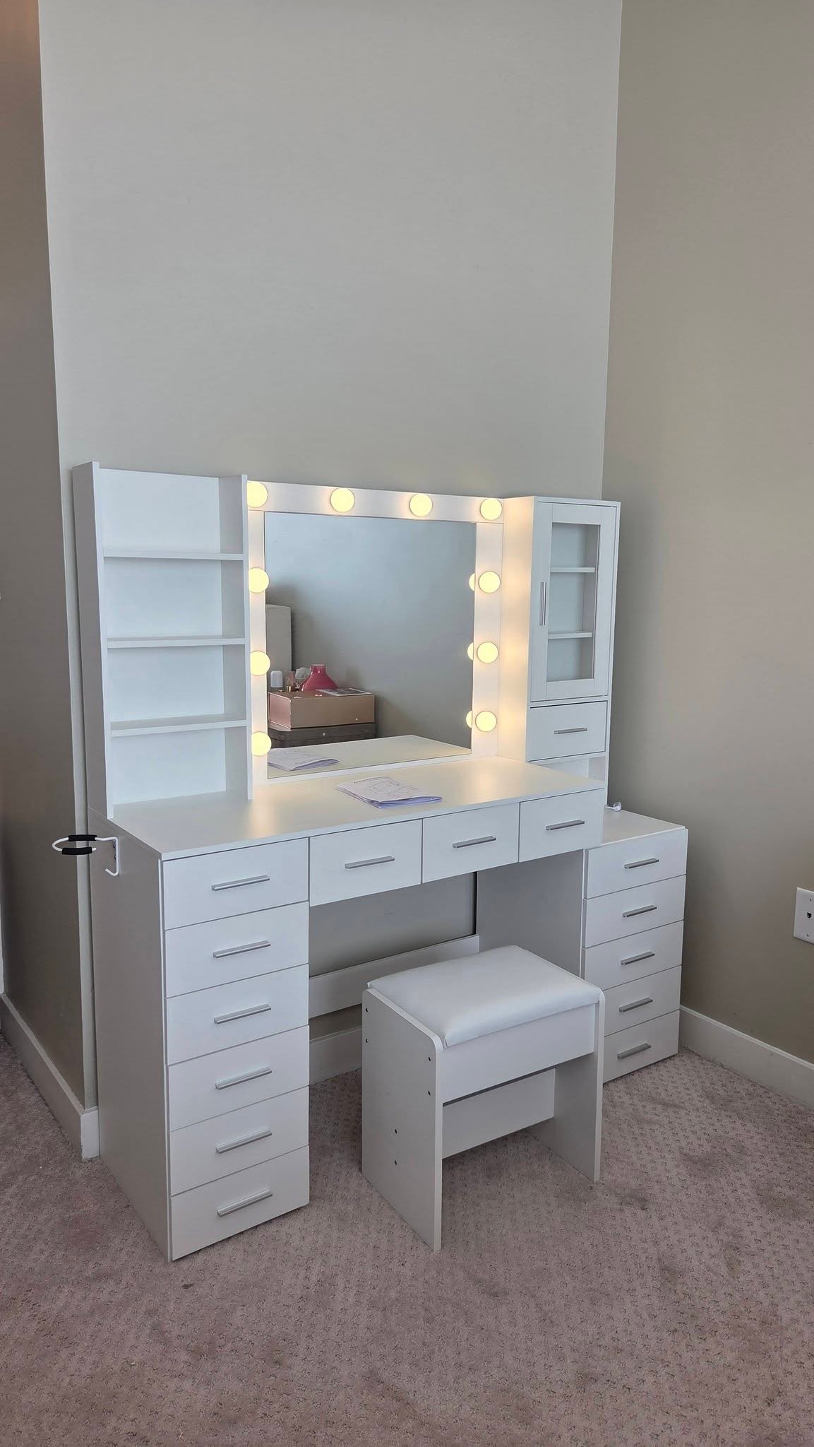 Finished white makeup vanity with multiple drawers, a lighted mirror, shelves, an upper cabinet and a matching stool